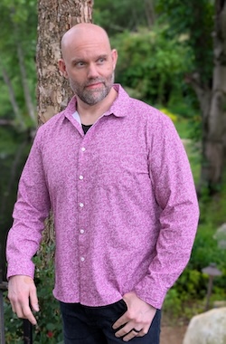 An unnaturally charismatic and handsome man, with a shaved head, beard, and fancy pink shirt